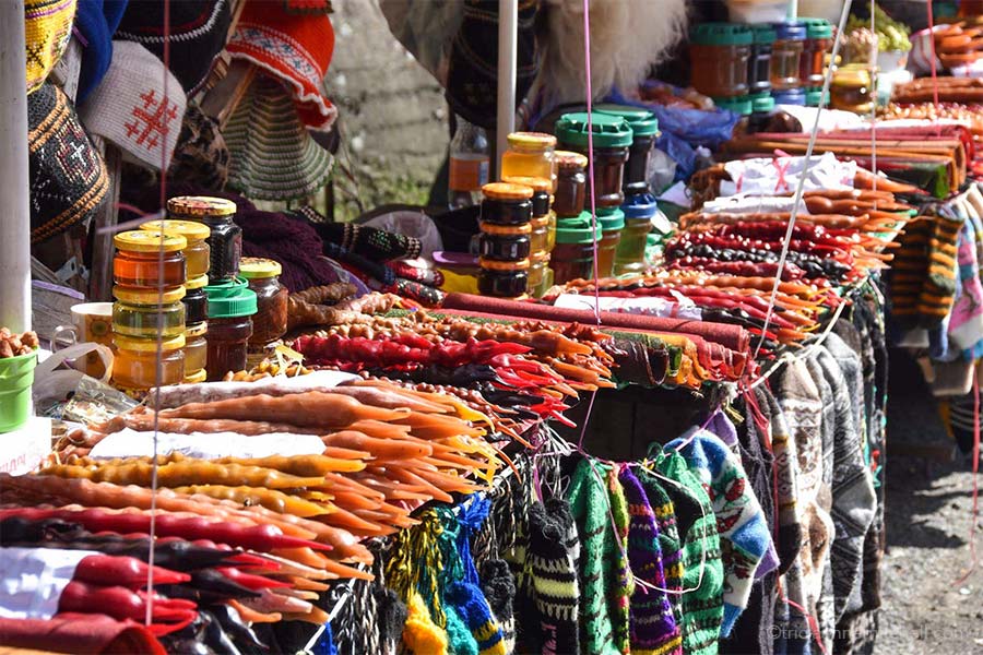 A table at a rest stop on the Georgian Military Highway is filled with handmade hats and socks, jars of honey, and red, brown, and yellow churchkhela treats.