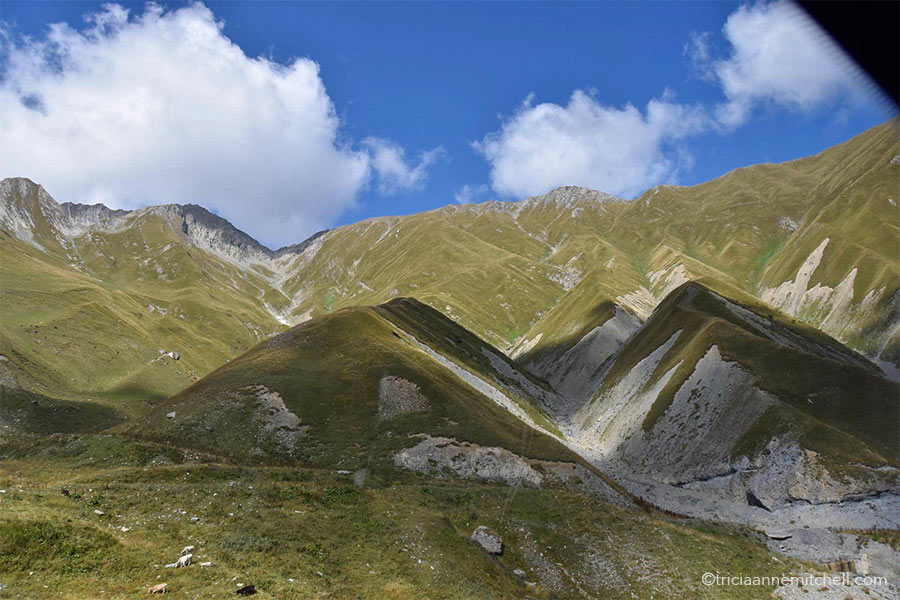 Clouds cast shadows on the green carpet-like slopes of the Caucasus.
