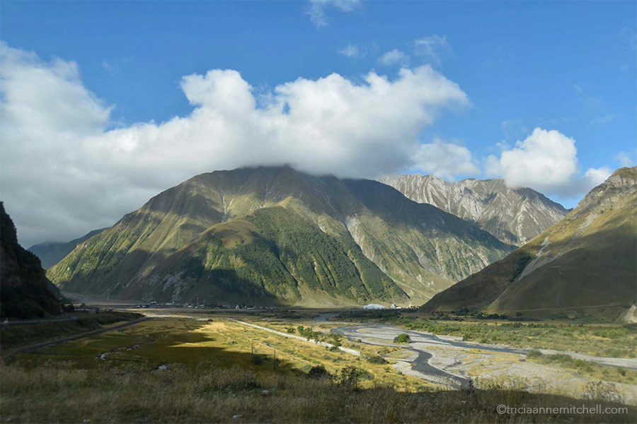 A river flows through the valley below a mountain covered with green vegetation near the Georgian Military Highway.