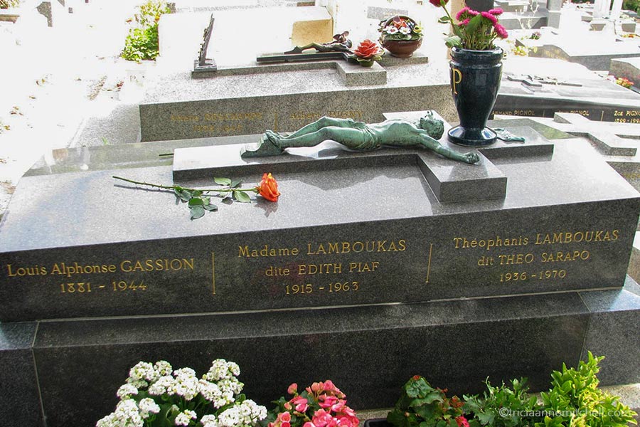 Edith Piaf's grave in Paris' Pere Lachaise Cemetery. There is a copper crucifix laying on top of the gray memorial and an urn filled with flowers is set on top of the memorial. The grave reads: "Louis Alphonse Gassion 1881-1944, Madame Lamboukas dite Edith Piaf 1915-1963, Theophanis Lamboukas dit Theo Sarapo 1936-1963"