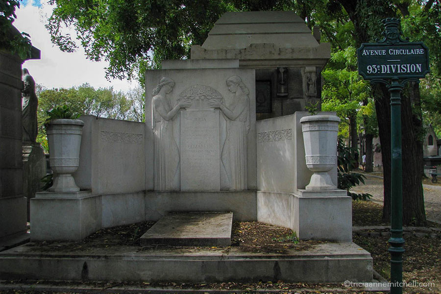 A white stone mausoleum features two women in long gowns holding a basket of flowers. To the right there is a sign that reads "Avenue Circulaire. 93rd Division."