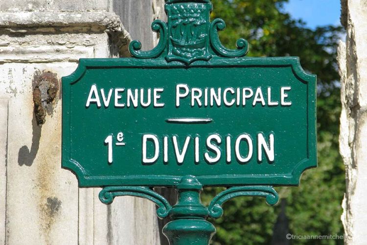 A decorative green iron sign in Pere Lachaise Cemetery reads: Avenue Principale 1e Division.