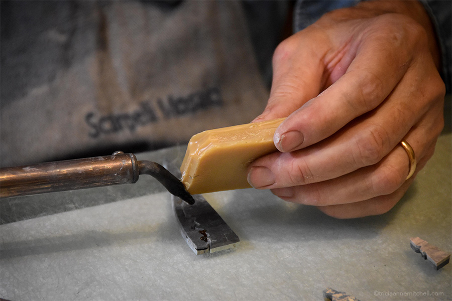 A master artisan melts a block of beeswax as he joins together two stone fragments.