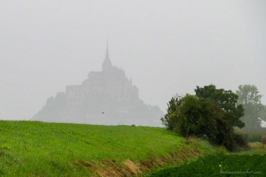 Mont Saint Michel looks silhouetted on a grey day.