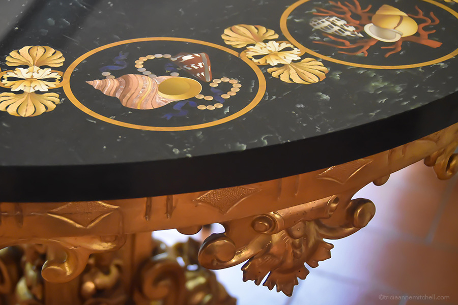 An ornate table at the Semi Precious Stones Workshop and Museum is predominantly black and gold with inlaid stone work depicting shells and coral.