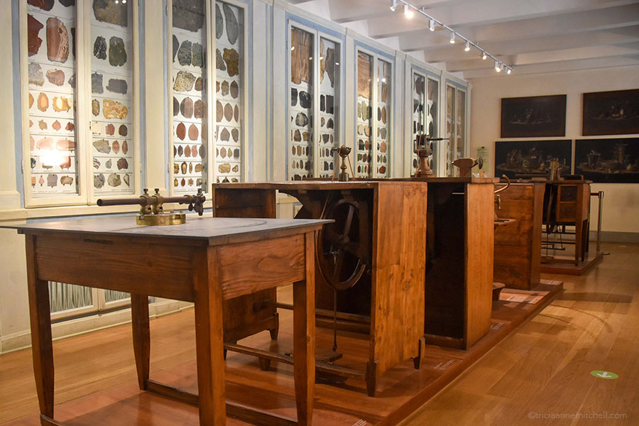 Wooden antique desks once used in a Florentine marquetry workshop sit next to glass cabinets filled with samples of semi-precious stones. This is one section of Florence's Opificio delle Pietre Dure Museum.