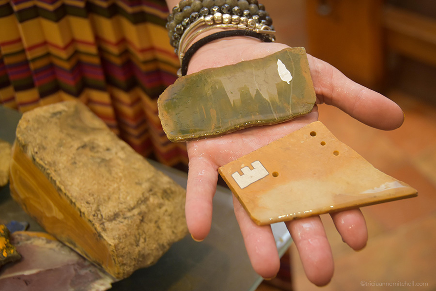 A woman shows two thin sheets of semi-precious rock, one green, one brownish-orange. They have adhesive stickers on them so the master artisan knows where to cut.