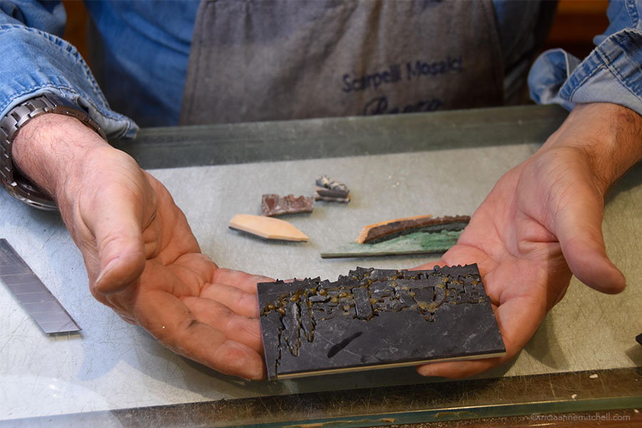 A master artisan holds an unfinished Florentine marquetry artwork. He's displaying the back of the piece so visitors can see how it's all glued together.