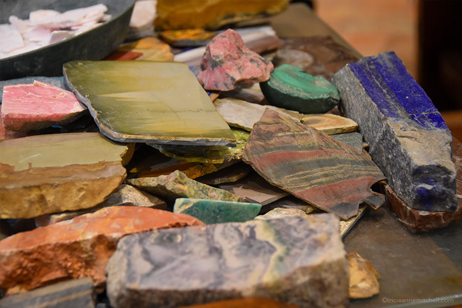A variety of semi-precious stone "shavings" sit on a master artisan's desk. They range from pink and green to blue and orange.