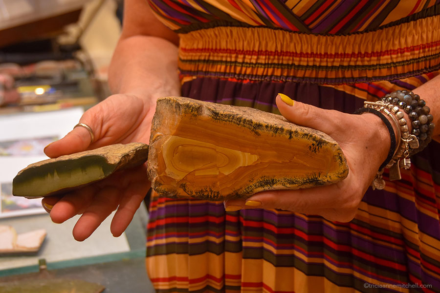 A woman in a master artisan's workshop holds two rocks as she explains the process of making Florentine mosaics / Florentine marquetry.