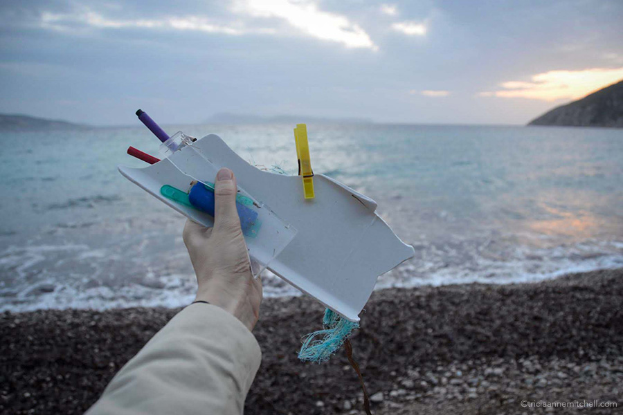 A hand holds plastic garbage picked up along a pebbly beach