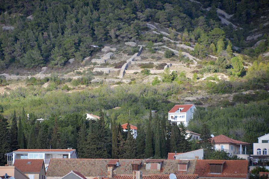 Hillsides overlooking a residential area. They have dry-stacked walls.