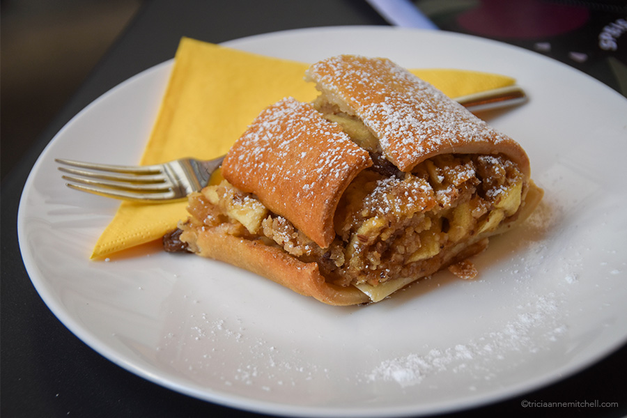 A slice of Strudel on a white plate, along with a napkin and fork.