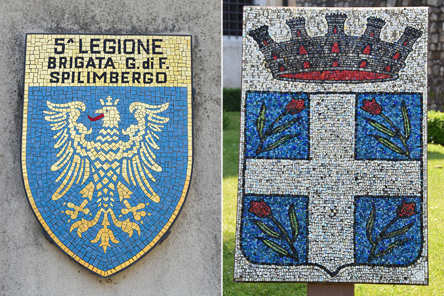 Two crests, crafted out of mosaics, are displayed outside. The mosaic on the left reads, "5 Legione Brigate G. di F. Spilimbergo" and features a golden eagle. The mosaic on the right features a black and red crown with four blue squares and red tulip-like flowers underneath.