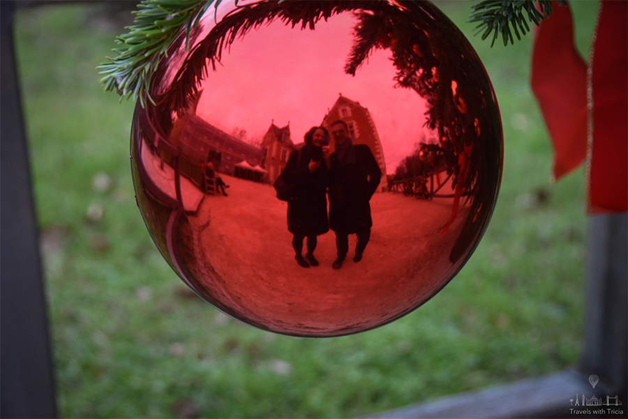 A couple is reflected in a red Christmas ornament.