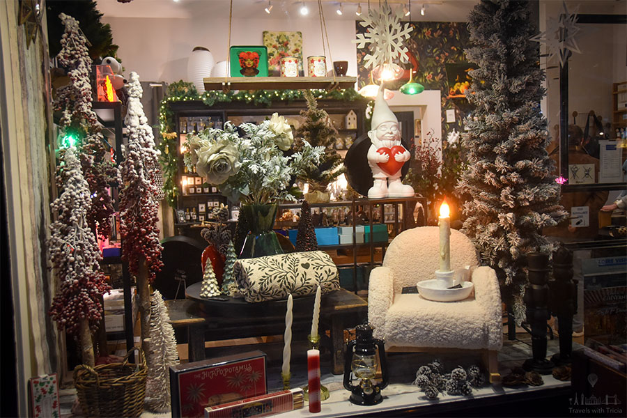 The storefront of the Petite Balade boutique in Amboise, France is decorated with a white gnome statue holding a heart, a fake candle, and artificial evergreen trimmings.