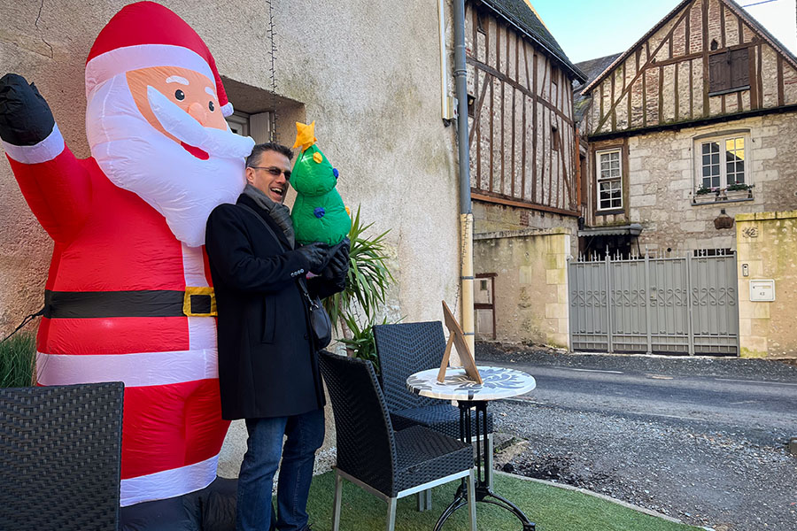 A man stands next to an inflatable Santa Claus in Amboise, France. A half-timbered stone building is in the background.