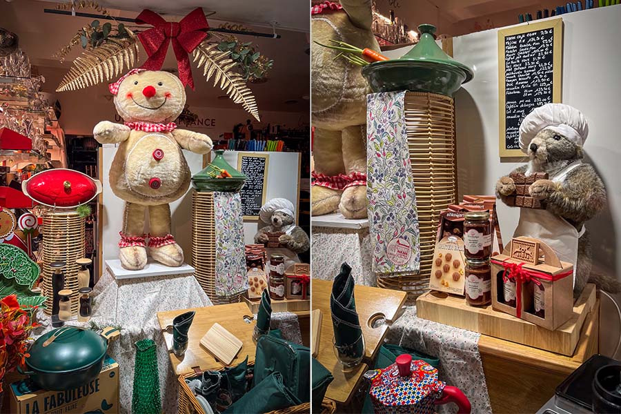 The "Un Coin de France" shop in Amboise, France is seen with Christmas decorations and chocolate products for sale in the window. There are green and red dishes, drinking glasses, and stuffed animals, including a woodchuck or marmot wearing a chef's hat.