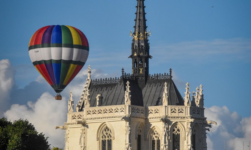A multicolored hot air balloon flies over the Chapel of Saint Hubert in Amboise, France, where Leonardo da Vinci's tomb is located.