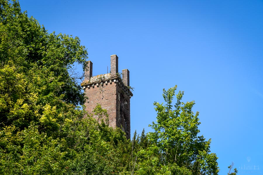 The Pile de Cinq Mars (a brick Gallo-Roman tower) rises above the treetops on a hillside in the town of Cinq Mars la Pile, France. The sky is blue with no clouds.