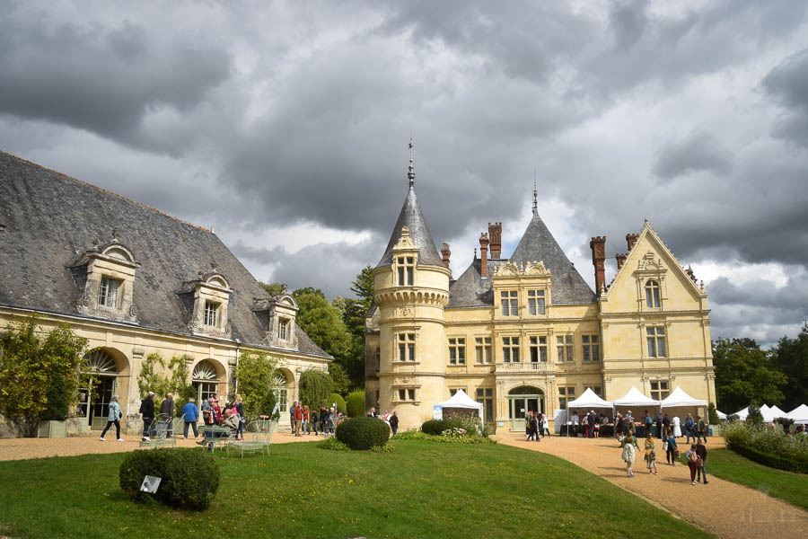 People walk the grounds of the Château de la Bourdaisière castle in France during the annual Tomato Festival. The castle's towers, dormer windows, and Renaissance architecture are visible under a grey sky and clouds.