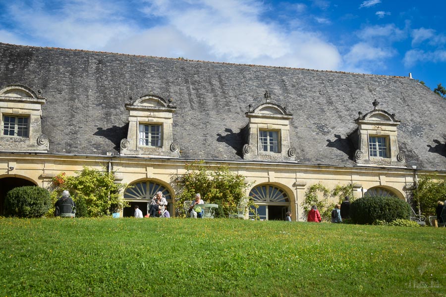 People sit on the grounds of the Château de la Bourdaisière in France. The sky is blue overhead and there is a green lawn.