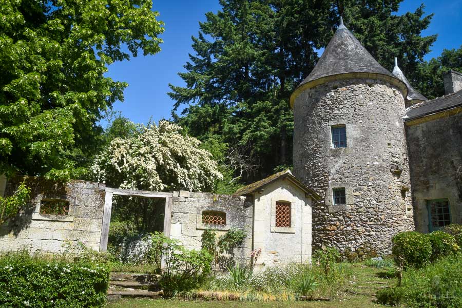 In the gardens of the Château de Cinq Mars, a stone tower and large trees overlook the rustic garden.