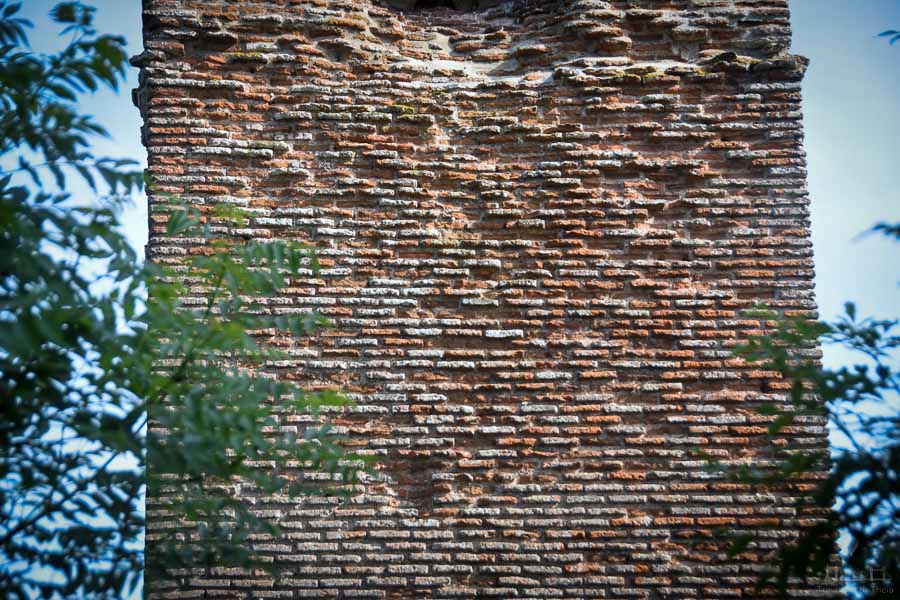 A close-up of a red brick face of the Pile de Cinq Mars in France. Tree branches fill the foreground of the photo.