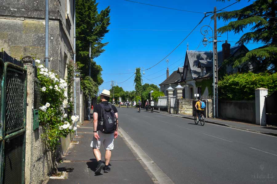 A man wearing a straw hat looks at white roses growing on the gate of a stone home in Cinq Mars la Pile, France.